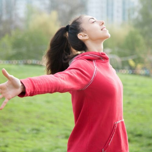 Profile portrait of happy sporty woman relaxing in park. Joyful female model relaxing, breathing fresh air outdoors with opened arms. Healthy active lifestyle concept